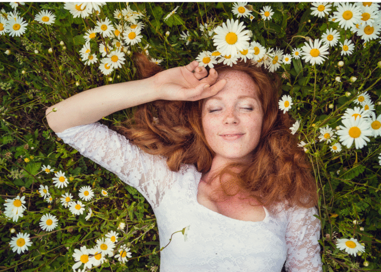 A woman reclines on a soft carpet of grass, surrounded by a picturesque meadow of white daisies in full bloom. Her serene expression and the tranquil setting evoke a sense of peace and well-being, perfectly capturing the spirit of spring wellness."