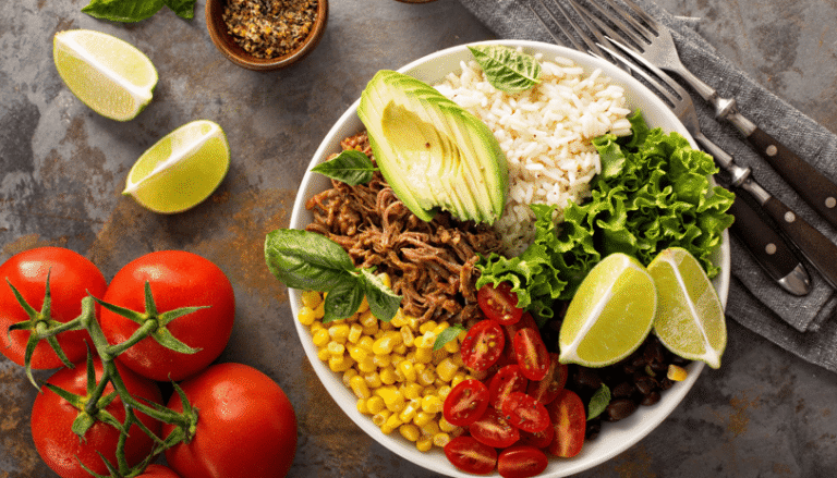 A bowl of pork carnitas garnished with avocado, tomato, and corn.