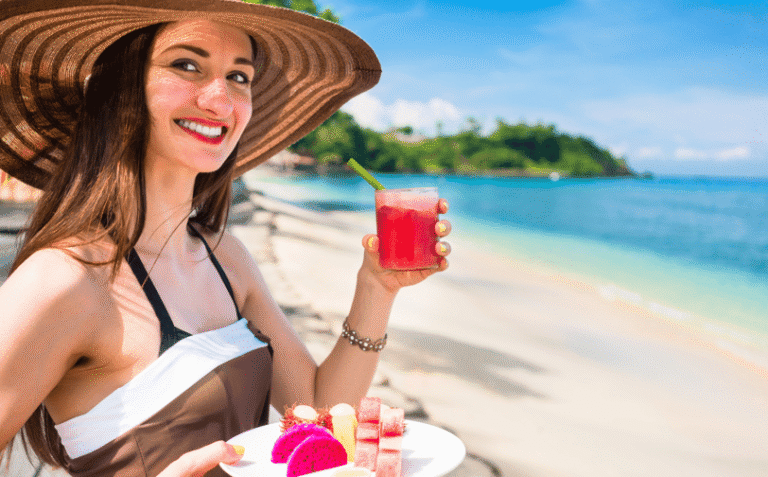 Smiling woman sitting by the beach sipping fruit juice.